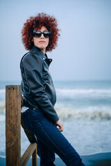 Portrait of an adult Arab woman with red curly hair in casual clothes in a beach at a rainy day