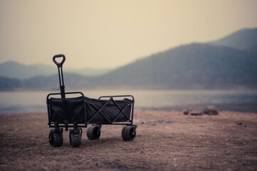 An empty black folding utility cart sits on the grassy shore. With the lake and sunset mountains serving as a tranquil backdrop.
