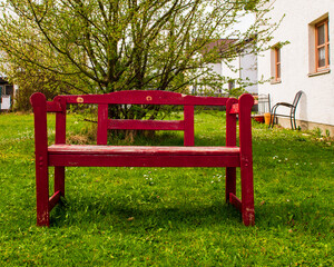 Old bench in garden in front of plum tree with red paint peeling off. Vintage park bench standing...