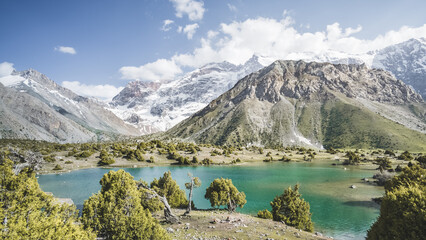 Panorama of mountain ranges and turquoise cold mountain lake on a warm sunny evening in the Fan...