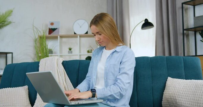 Young woman student working on laptop while writing university home task sitting on couch at home