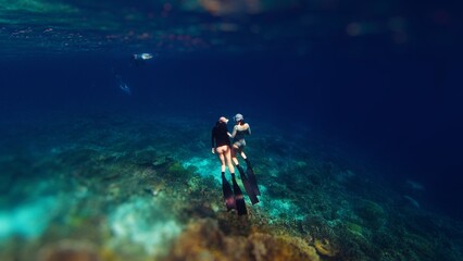 Two female freedivers swim underwater in the tropical sea and enjoy the healthy coral reef in the...