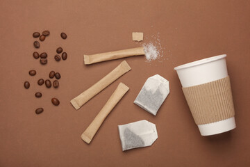 Cardboard cup, Coffee beans, tea bags and disposable sticks with sugar on a beige background. Flat lay