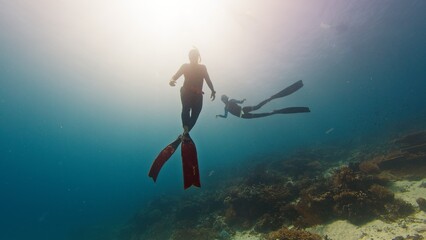 Two male freedivers swim underwater and explores vivid and healthy coral reef in Komodo National Park in Indonesia
