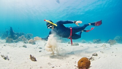 Male freediver glides in the tropical sea over the sandy bottom and plays with sand