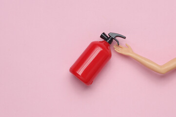Doll hand holding Toy extinguisher on pink pastel background. Top view