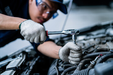 A mechanic is working on a car engine, using a socket wrench to loosen a bolt. Concept of focus and...