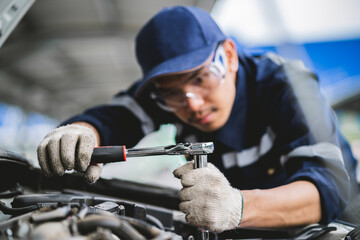 A mechanic is working on a car engine, using a socket wrench to loosen a bolt