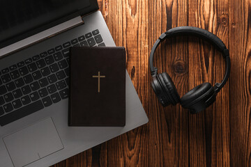 Bible book with laptop and headphones on a wooden table. Online Bible study