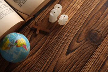 Bible book, candles and wooden Christian cross on a string, globe wooden table. Messianism,...