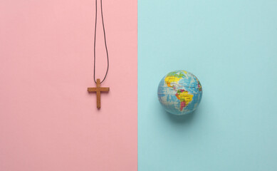 Wooden Christian cross on a string with globe on pink blue background. Messianism, Christian...