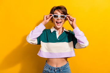 Photo of positive impressed lady dressed polo shirt hands dark eyewear smiling isolated yellow color background - obrazy, fototapety, plakaty