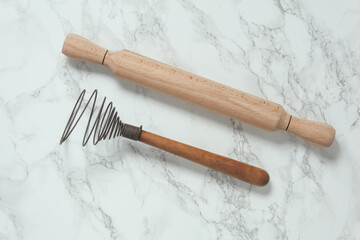 Wooden rolling pin and whisk on marble background