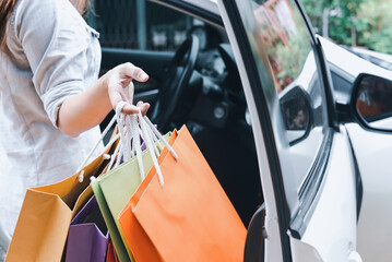 Close-up of a woman's hands placing colorful shopping bags into a white car after a shopping spree..