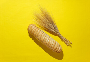 Baguette and spikelets of dry wheat on a yellow background