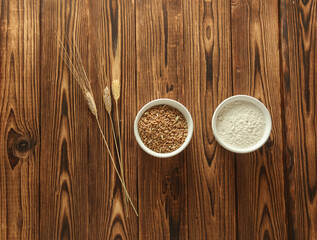 Spikelets of wheat, grains and flour in bowl on wooden table