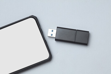 Smartphone and black USB flash drive on a gray background