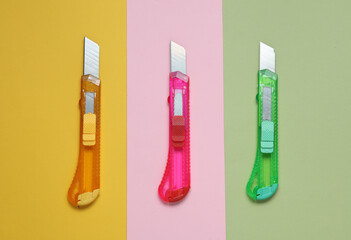 Plastic colored stationery knives for cutting paper on pastel background