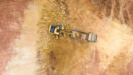 Aerial view of an excavator and crane loading crushed red rocks and sand. Trucks at work,...