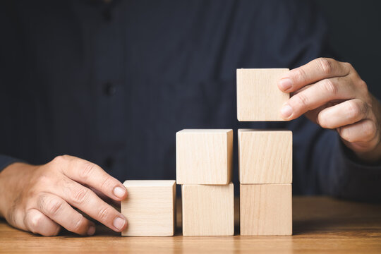 Man playing wooden cubes, arrange it as step stairs on the table, business plan concept, improvement, career progress, build a success