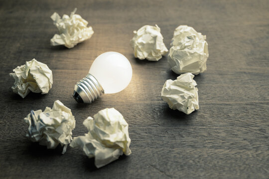 Small light bulb glowing among the crushed paper balls, usable idea, original, creativity, and learning concept