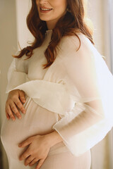 Close up photo of happy pregnant woman in stylish ivory transparent dress in the studio. Happy...