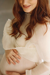 Closeup photo  of attractive pregnant woman in stylish ivory dress in the studio. Stylish...