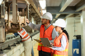 Male and female engineers work together in an electric repair station. Inspecting the undercarriage of electric train that are being repaired at the garage.