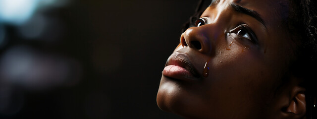 Young black woman looking up praying to God with tears in eyes, being touched by His Grace. Christian and faith concept. - obrazy, fototapety, plakaty