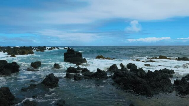 Waves slowly splash on black lava rocks at a volcanic beach in Keanae Penisula, Maui. Cloudy day at the volcanic beach.