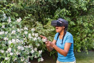 woman with virtual reality goggles pointing at garden plants. Augmented reality Concept.