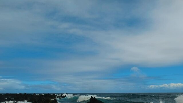 Tilt shot of the waves slowly splashing on black lava rocks. Cloudy day at the volcanic beach in Keanae Penisula, Maui.