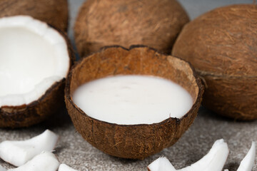 Fototapeta na wymiar Coconut milk in coconut shell and half coconut, chopped flesh on grey background