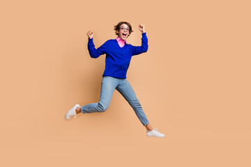 Full body portrait of overjoyed pretty lady jump raise fists success empty space isolated on beige color background