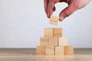 Hand Placing Wooden Block on a Pyramid Structure
