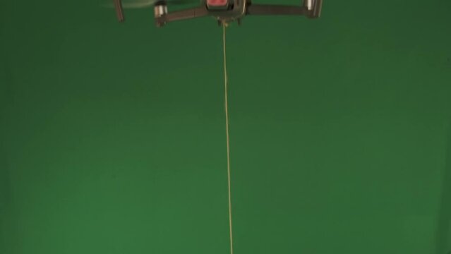 Flying drone lowers a gift on a string in red holiday packaging on a green chromakey background. Delivering holiday gifts using modern flying quadcopter technology