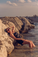 Fototapeta na wymiar A young beautiful girl posing on a rocky sea beach in a short black dress