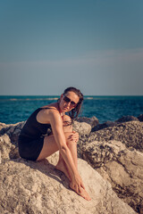 A young beautiful girl posing on a rocky sea beach in a short black dress