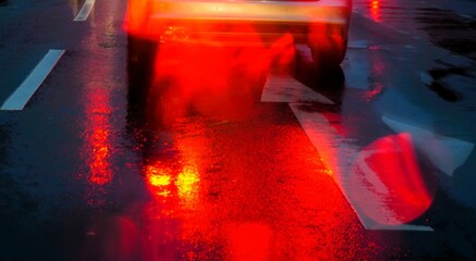 Abstraktes Motiv von Auto auf Straße mit weißem Pfeil und rot-gelben Lichtern und Spiegelung auf...