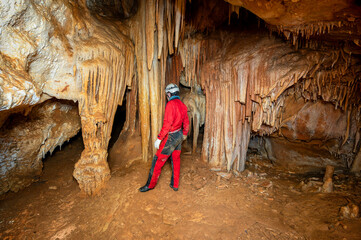 A speleologist with helmet and headlamp exploring a cave with rich stalactite and stalagmite...