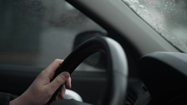 Driving car on rainy cloudy city road, hands holding the steering wheel. close-up of a man's hand on the steering wheel while driving a car in rainy cloudy weather. Closeup male hands driver on city.
