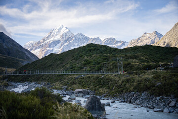 Tourists crossing swing bridge above glacial river in alpine environment, Mt Cook, New Zealand