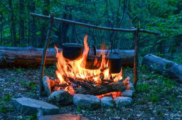 Smoky cauldrons on a fire in a tourist camp against the backdrop of an evening forest. Cooking while camping.