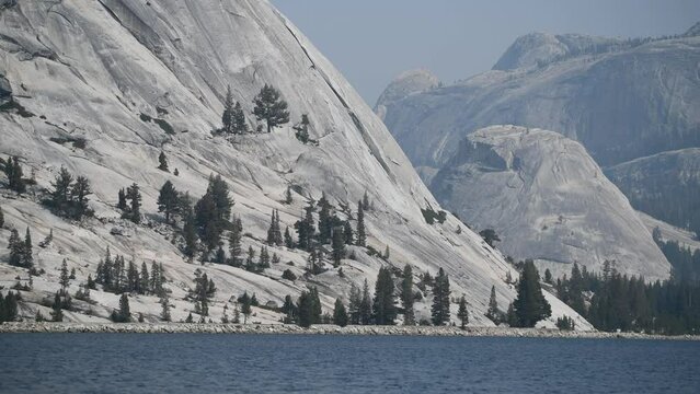 Closeup of the coast of Lake Tenaya and the mountains of gray rocks and patches of trees that surround it. View during the 2021 California wildfires