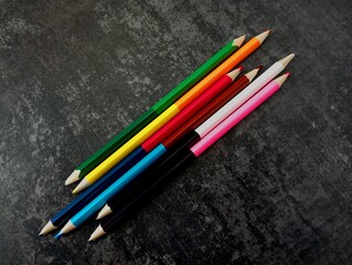 A group of pencils laid out on a dark concrete background. Colored pencils with different colors on...