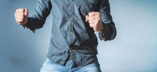 A man in a blue shirt and jeans is holding and clenching his fists up in the air. on blue background
