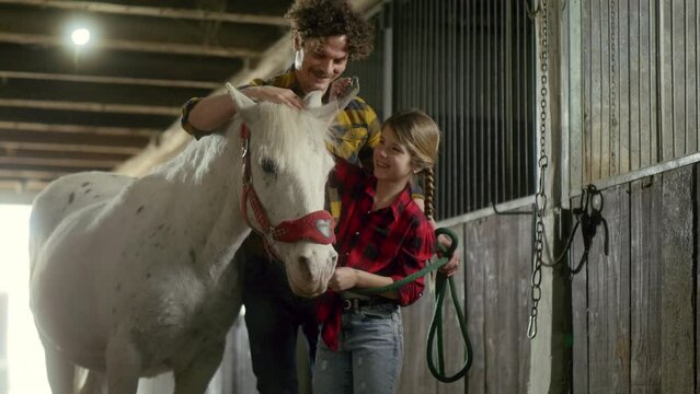 Farmer and his little daughter brush a horse in the barn, a father teaches his daughter to take care of his horse