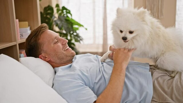 Young caucasian man with dog smiling confident lying on bed playing at bedroom