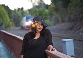 An overweight fashionable Indian woman from South Asia waits for an approaching train.