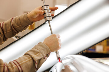 Mechanic removing dents from car body using bright lamp and specialistic equipment. Mechanic's and car repair studio.